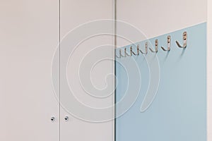 Metal hooks on light blue wall near white wardrobe in modern office. Minimalist style design.