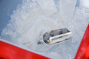Metal ice scoop and plastic cup on the ice in bucket