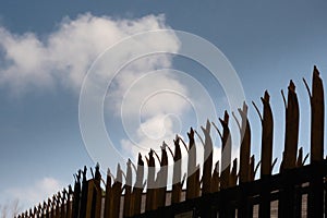 Metal industrial security fence with spikes on top against blue sky background.