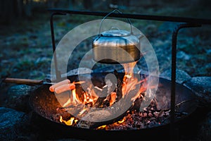 Metal kettle and grilled sausage on a campfire