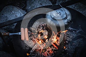 Metal kettle and grilled sausage on a campfire
