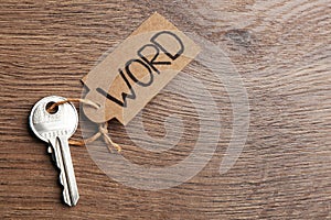 Metal key with tag on wooden table, top view and space for text. Keyword concept