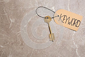 Metal key and tag wIth word KEYWORD on grey table, top view. Space for text