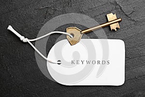 Metal key and tag wIth word KEYWORDS on black table, top view