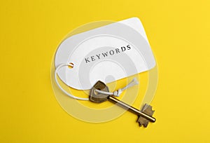 Metal key and tag wIth word KEYWORDS on yellow background, top view