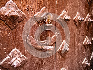 Metal knocker on an old wooden door and surrounded by deterrent skewers