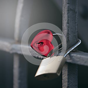 Metal lock in the form of a red heart hangs on the metal structure of the bridge close up, as a symbol of love.