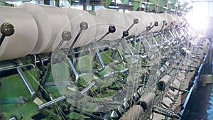 Metal machines work with threads at a textile factory, coiling them onto bobbins.