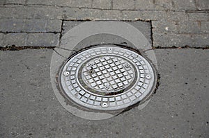 Metal manhole cover on rough cobblestone and asphalt street