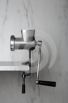 Metal manual meat grinder on table against white marble background