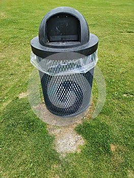 Metal mesh trash can at the park with plastic bag filled with trash