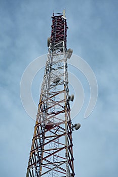 Metal mobile communications tower cell site with antennas close-up against the sky at dusk. Vertical orientation.