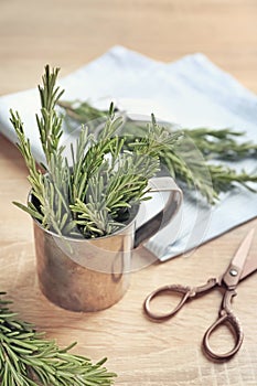 Metal mug with fresh rosemary on wooden table