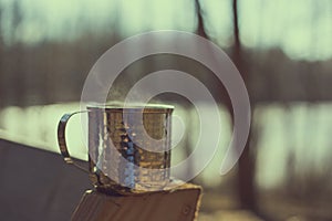 Metal mug holding hot liquid in woods