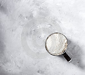 Metal mug sieve with wheat flour. On a gray background. View from above