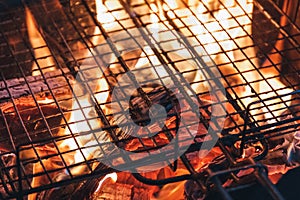 Metal net over fire burning coal ember wood in barbecue grill at