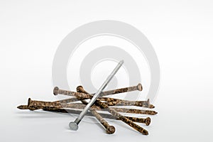 Metal new nail on a pile of old rusty nails on a white background. The concept of a new solution, look, uniqueness