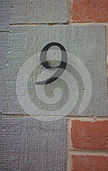 Metal number nine or 9 coated with black paint applied in Latin letters to the building.