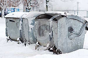 Metal old garbage cans are standing in the yard in the snow in winter