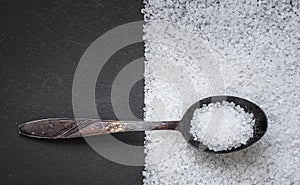 Metal old spoon with coarse sea salt on a dark background