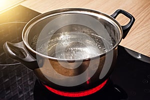 Metal pan with boiling water on the induction cooker red hot plate.