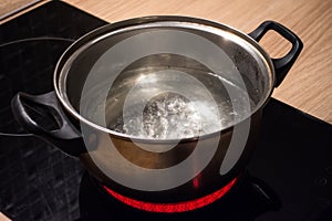 Metal pan with boiling water on the induction cooker red hot plate.