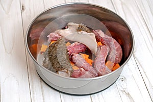 Metal pet bowl with chicken necks, beef paunch pieces and cut carrot.