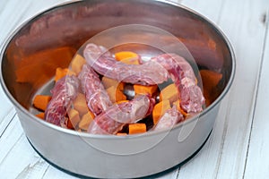 Metal pet bowl with chicken necks and cut carrot inside. Beginning of natural organic daily meal ration preparation, BARF diet for