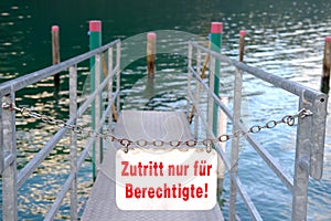 Metal pier with a railing is closed with a chain. A white sign in German hangs: entrance only to beneficiary, resort place.