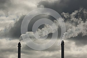 metal pipes of the plant against a gray sky, gray smoke comes out of the pipes