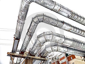 Metal pipes in thermal insulation winding outdoors and the over-illuminated white sky on the background