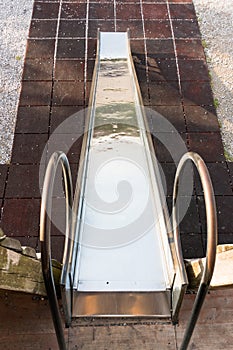 Metal playground slide going down onto a red mat ground