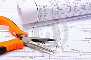 Metal pliers and rolled electrical diagram on construction drawing of house