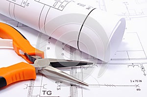 Metal pliers and rolled electrical diagram on construction drawing of house