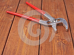 Metal plumber wrench with red handles on wooden surface