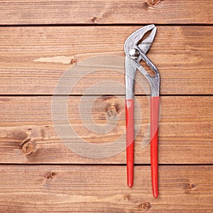 Metal plumber wrench with red handles on wooden surface