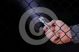 Metal pocket flashlight in a man`s hand on a black background, a beam shines in the dark, prison bars, the concept of light in th