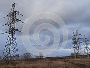 Metal pylons of a power line against a disturbing cloudy sky on the outskirts of a city. High voltage towers. Desolate