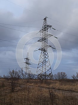 Metal pylons of a power line against a disturbing cloudy sky on the outskirts of a city. High voltage towers. Desolate