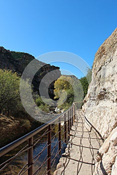 A metal railing along a trail carved into a mountainside along a creek in the mountains