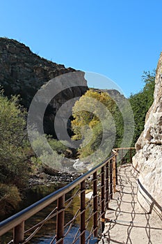 A metal railing along a trail carved into a mountainside along a creek in the mountains of the Sonoran Desert