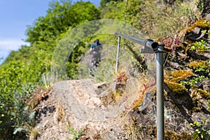 Metal railing on the trail in wineries, visible plants growing on slate and a man in the background.