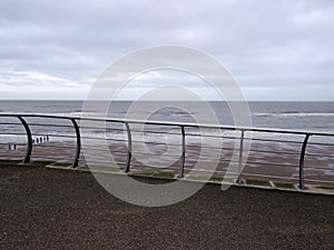 Railings on the seafront in blackpool with waves breaking on the beach under a cloudy sky