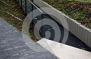 Metal ramp for wheelchairs made of dark gray lattice and retaining wall at the flowerbed made of prefabricated concrete palisade o