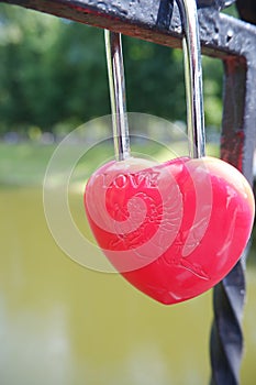 Metal red door lock in the shape of a heart on the fence as a symbol of eternal love.