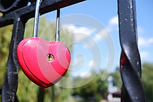 Metal red door lock in the shape of a heart on the fence as a symbol of eternal love.