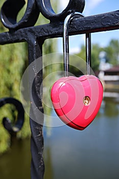 Metal red door lock in the shape of a heart on the fence as a symbol of eternal love.