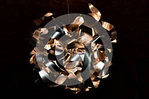 Metal ribbon chandelier closeup. Modern lampshade. Copper and silver textured background. Abstract chaotic pattern.