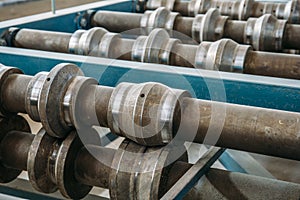 Metal rolls of roll forming machine close up at sandwich panel factory or metalwork manufacturing