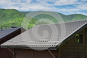 Metal roof construction on a wooden house against a background of mountains. Rain gutter.